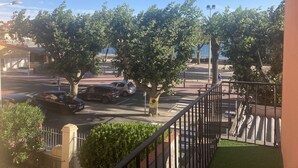 A balcony with a view of a street lined with trees, parked cars, and a distant body of water. - Hôtel Les Pêcheurs (Banyuls-sur-Mer)