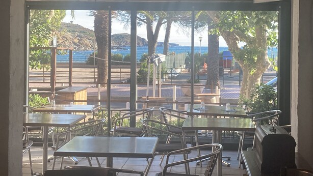 An outdoor dining area with tables and chairs, overlooking a coastal landscape with trees and a view of the sea. - Hôtel Les Pêcheurs (Banyuls-sur-Mer)