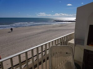 A beach view from a balcony with a railing, a chair, and a building with a window. - Charming 1-BR in Palavas - Direct Beach Access, Parking (Palavas-les-Flots)