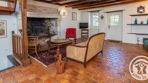 A rustic interior with exposed wooden beams, a fireplace, a red armchair, and a television. - Charming house with enclosed garden near the Louet river (Denée)