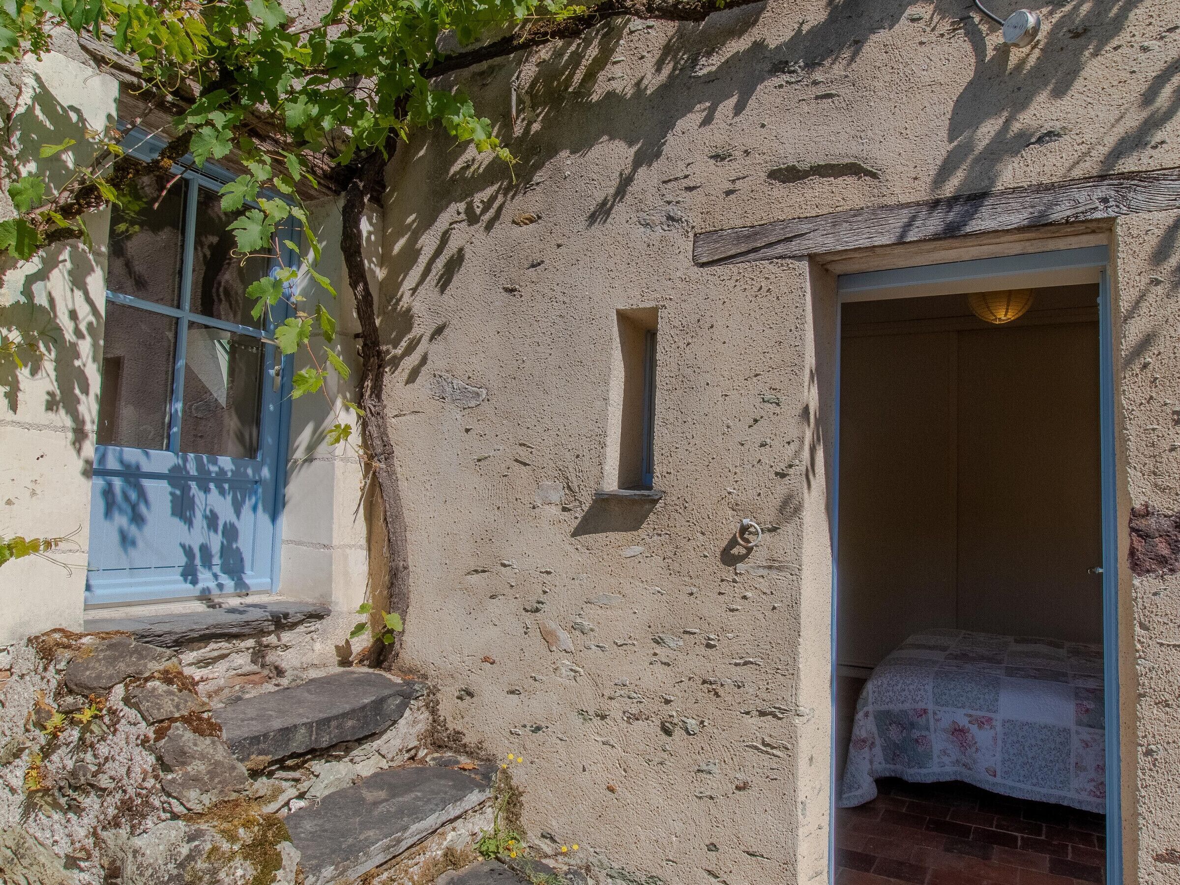 A rustic stone building with a small window and a door leading to a room with a bed.