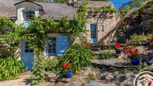 A stone house with a blue door and window shutters, surrounded by lush greenery and potted red flowers. - Charming house with enclosed garden near the Louet river (Denée)