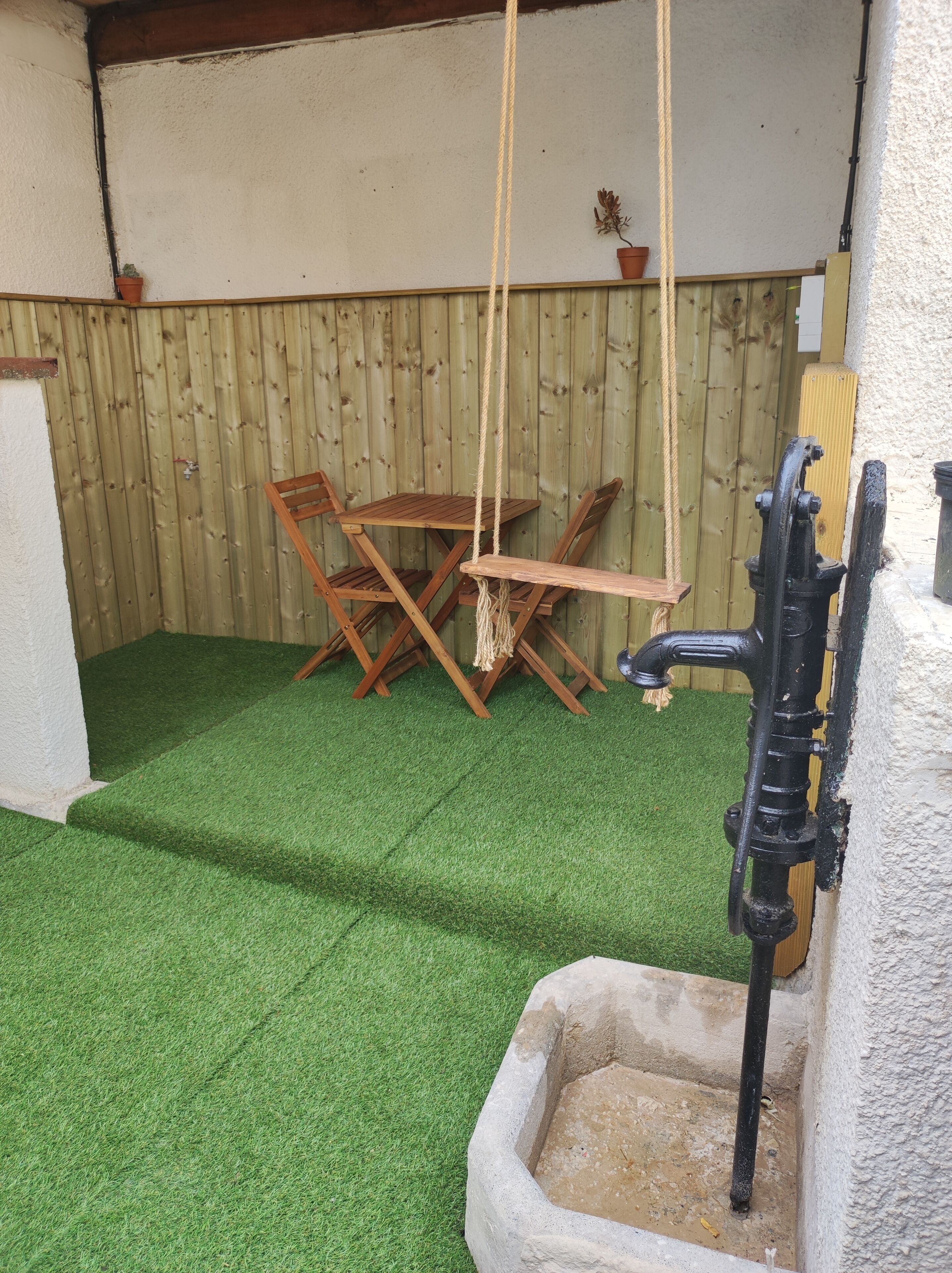 Une terrasse avec un revêtement de gazon synthétique, des meubles en bois et un élément décoratif aquatique.
