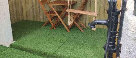 Une terrasse avec un revêtement de gazon synthétique, des meubles en bois et un élément décoratif aquatique.