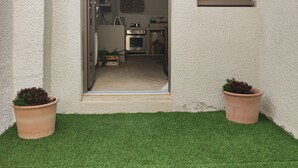 Entrada de una casa con un pequeño patio, una cocina visible a través de la puerta abierta, y dos macetas a cada lado.