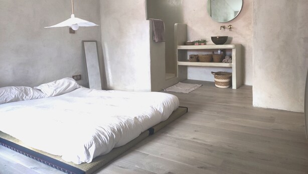 Un dormitorio con una cama grande, una lámpara colgante, un espejo y un estante empotrado con cestas.