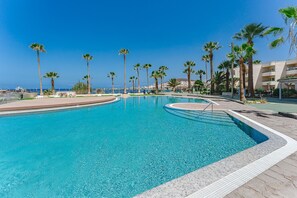 Une grande piscine d’un bleu éclatant, entourée de palmiers, avec une vue sur l’océan.