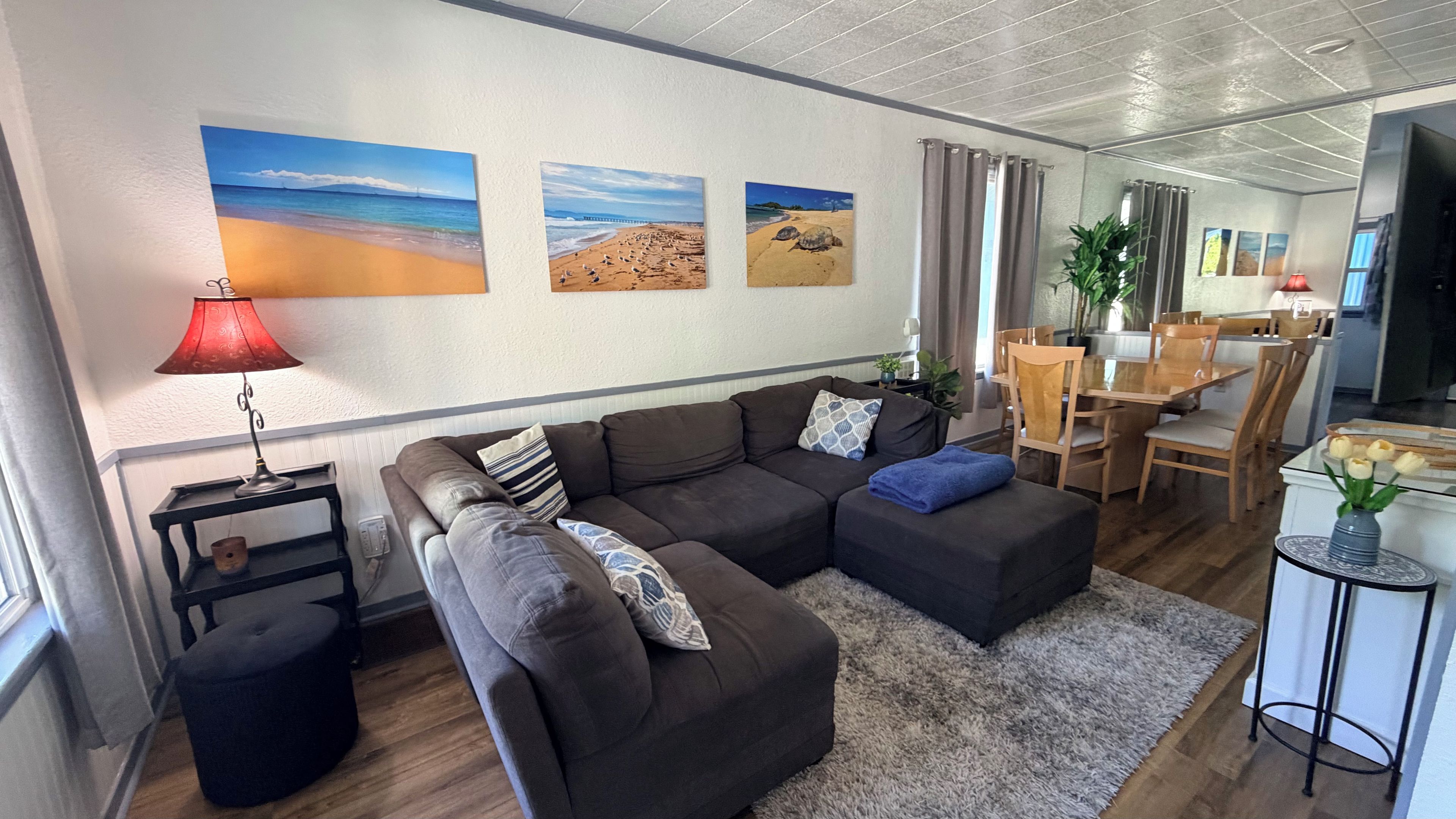 A modern living room with a sectional sofa, a dining area, and artwork depicting beaches.