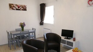 Un soggiorno con un tavolo da pranzo, due sedie, una TV e un piccolo tavolino con frutta e una scatola decorativa.