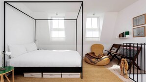 A modern bedroom with a four-poster bed, a small side table, a chair, and a bookshelf. - The Brickworks, by Veeve (London)