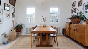 A dining area with a wooden table, chairs, a vase with flowers, and a potted plant. - The Brickworks, by Veeve (London)