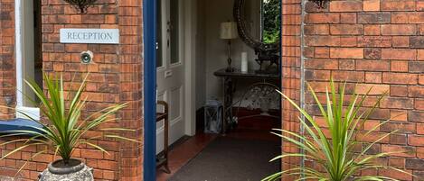 A reception area with a sign, a blue door, hanging flower baskets, and two potted plants.