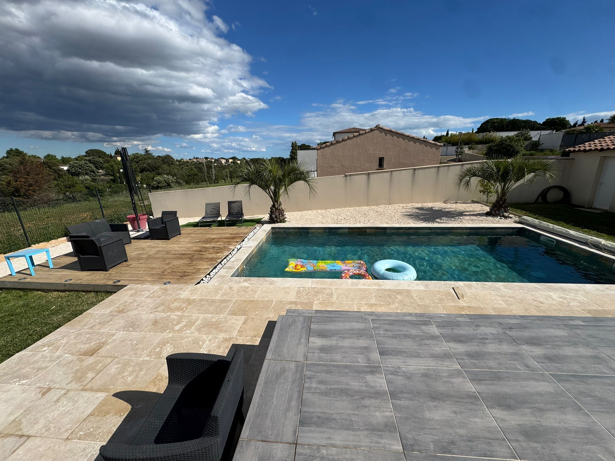 Una piscina con sillas de descanso, un muelle de madera y un patio de piedra.