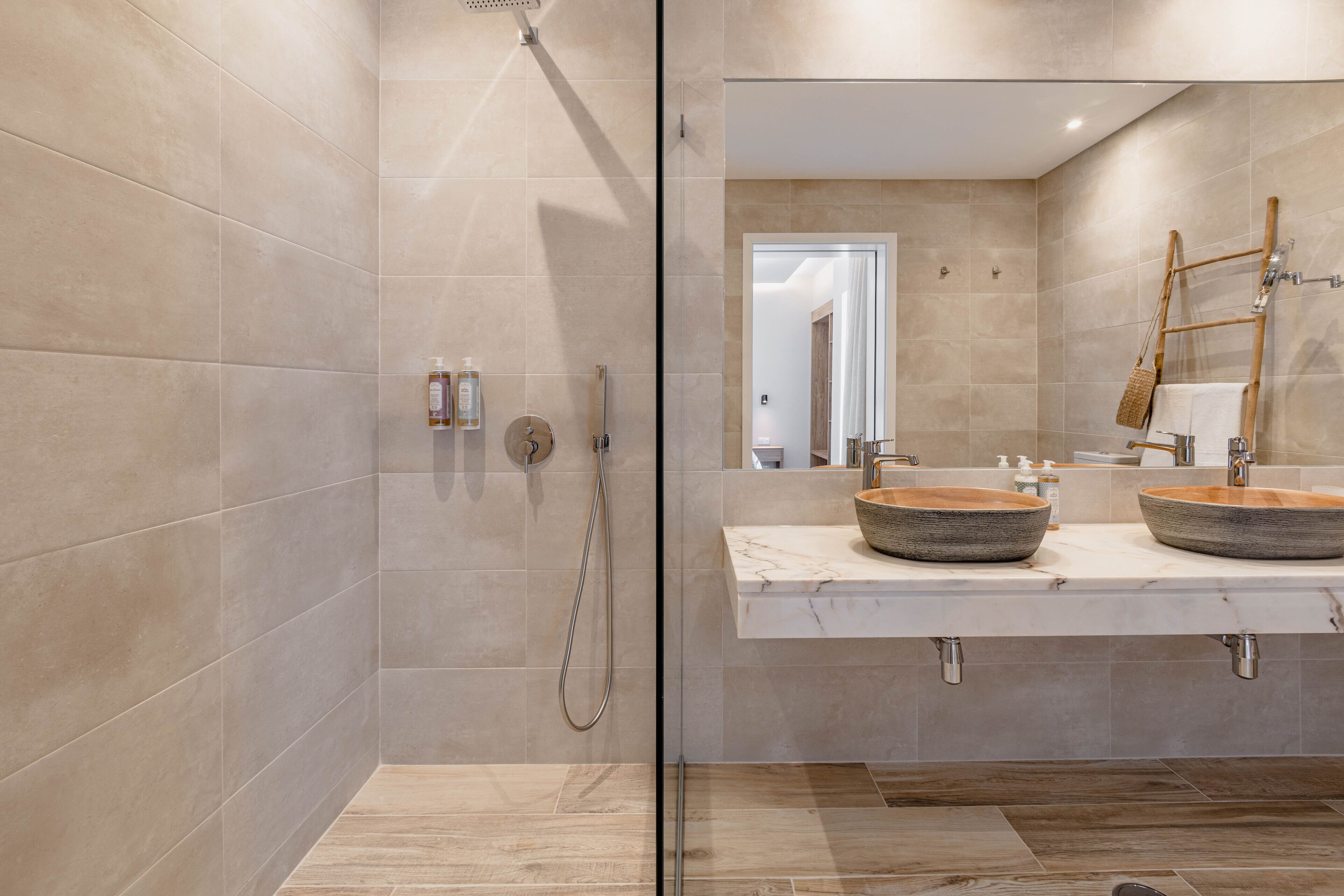 Une salle de bain moderne avec une douche à parois de verre, deux vasques et un escabeau en bois.