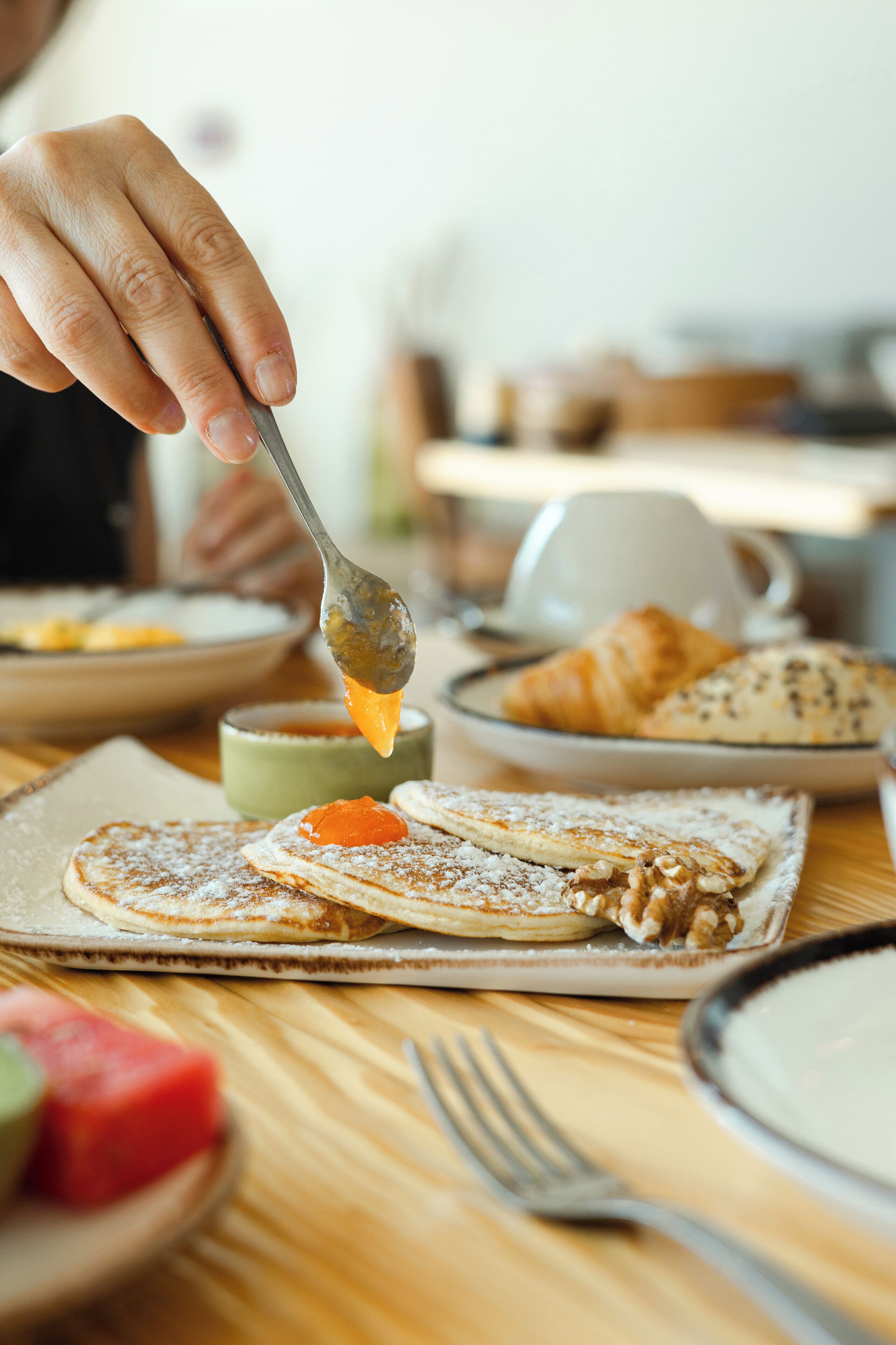 Uma mesa de madeira com panquecas, um croissant e uma xícara de café.
