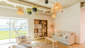 Een moderne woonkamer met een bank, stoelen, een salontafel en een boekenkast. Er is een groot raam met uitzicht op het omliggende landschap.
