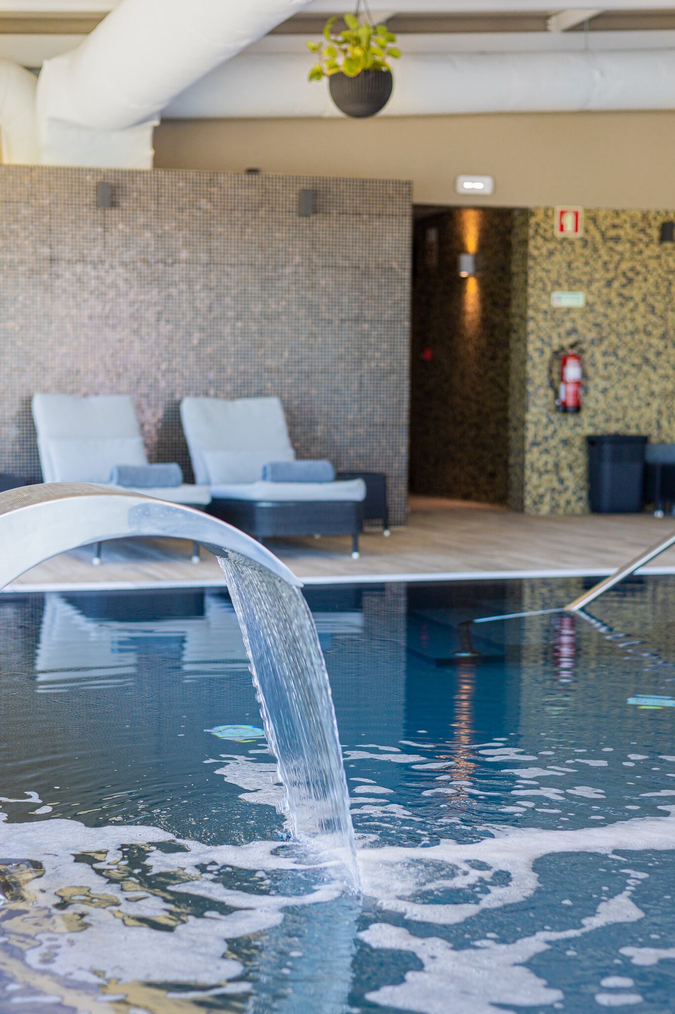 Una piscina con fuente, sillas de descanso y pared con textura.