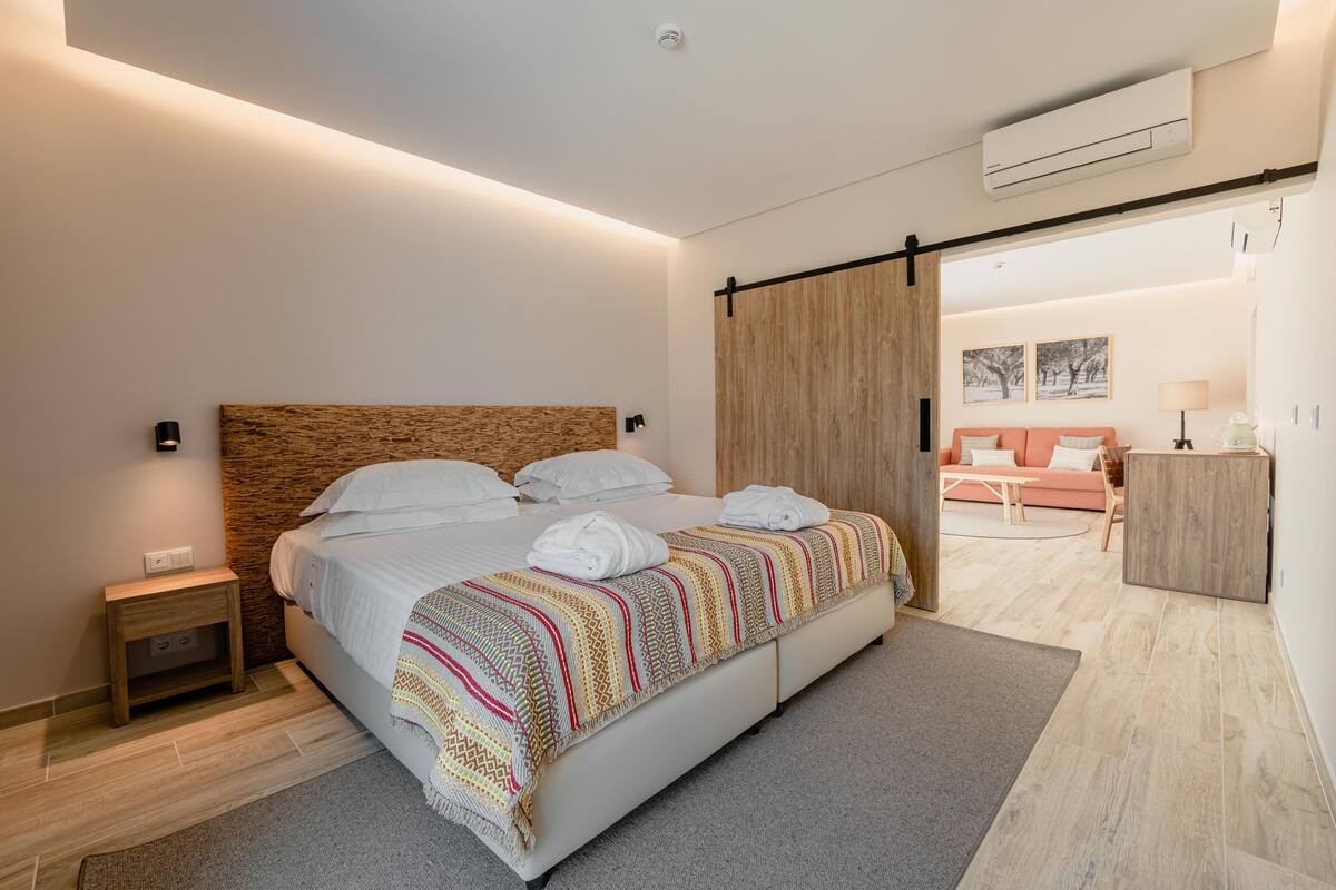 Un dormitorio moderno con una cama grande, cabecera de madera, una mesita de noche y una puerta corredera que da a una zona de estar.