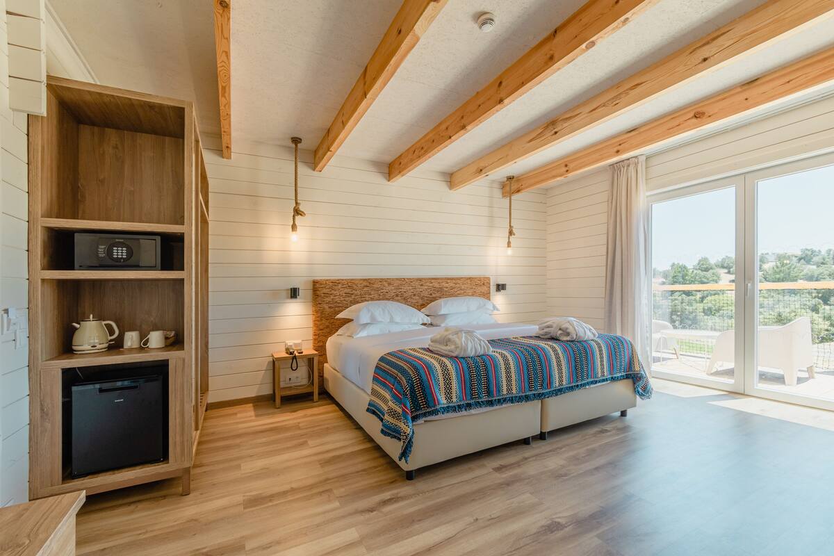 Un dormitorio con techo de madera, una cama con manta colorida, una mesita de noche pequeña y un mueble empotrado para la televisión.