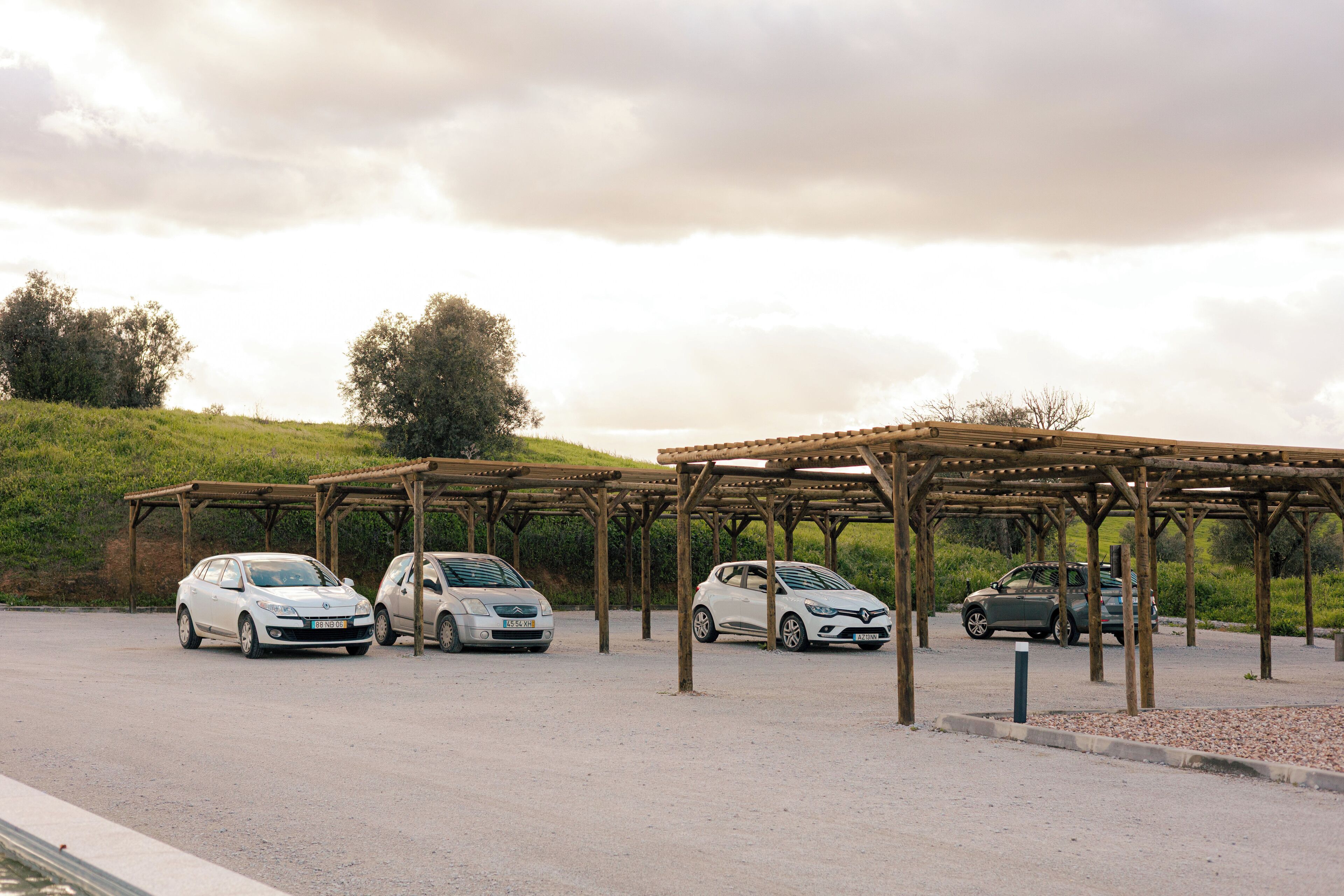 A parking area with covered car parking spaces and a grassy hill in the background.