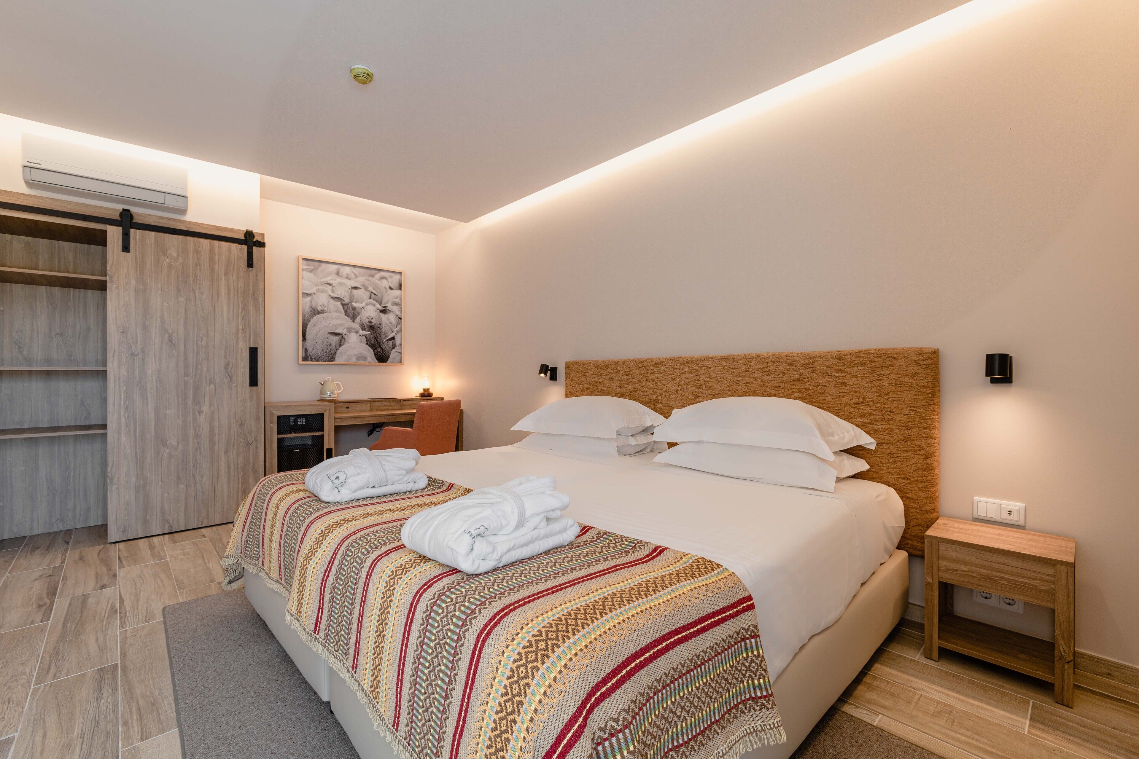 Una habitación de hotel moderna con una cama grande, un cabecero de madera, una mesita de noche, un escritorio y un armario.