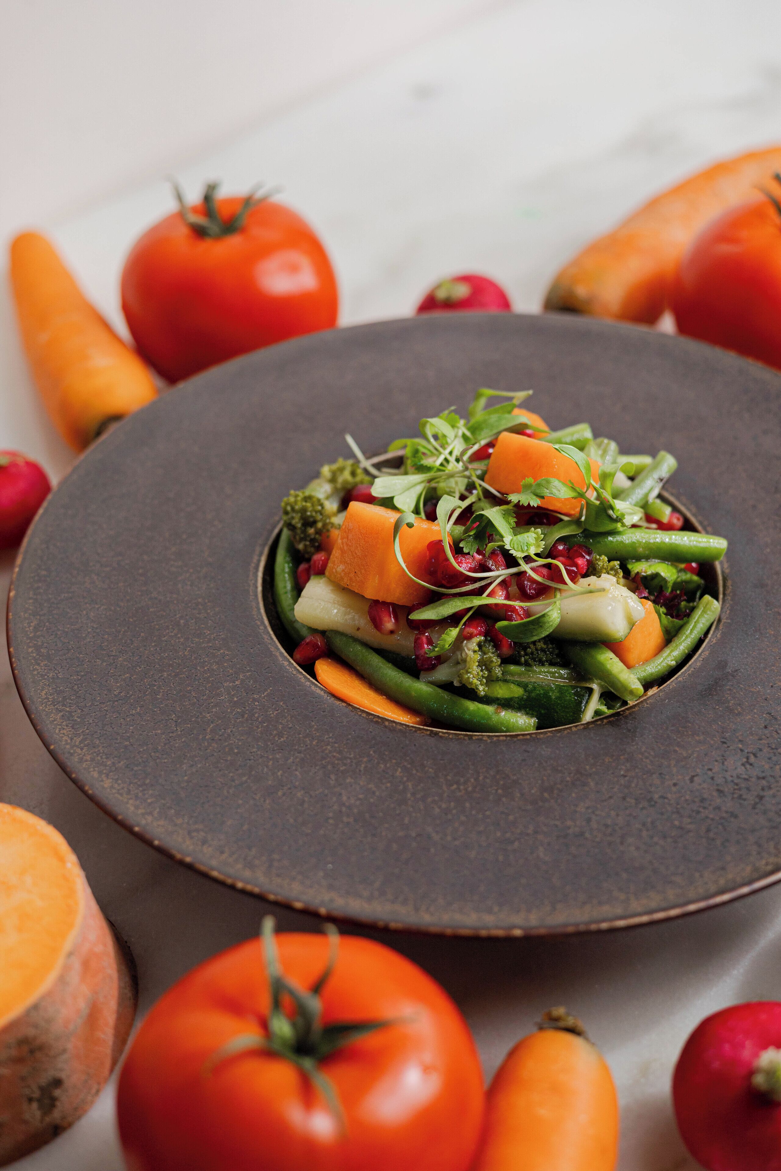 Un tazón con vegetales variados sobre un plato oscuro.