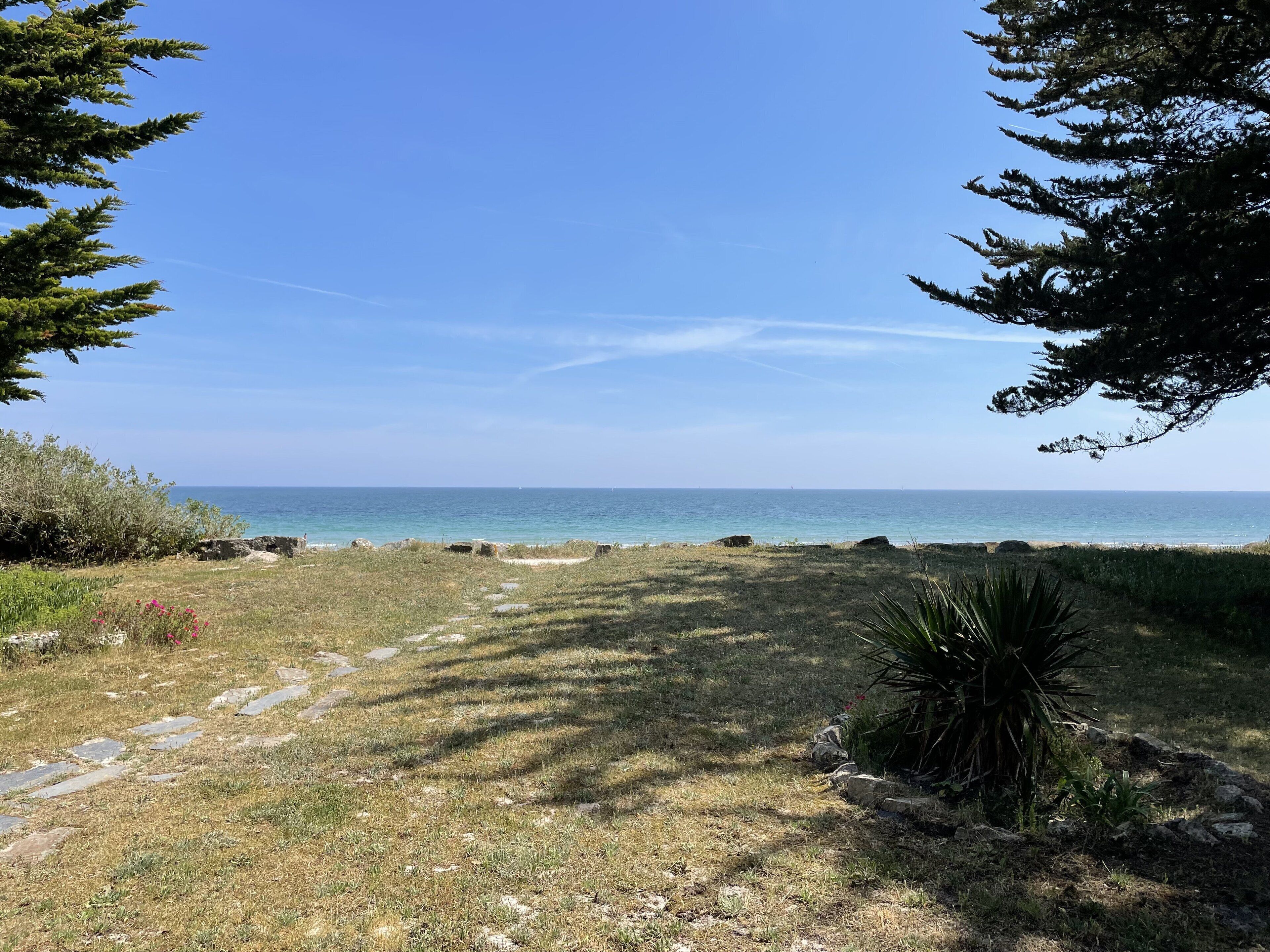 A coastal path leading to the sea, surrounded by greenery and rocks.