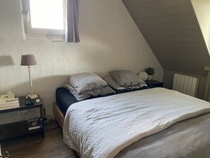 Une chambre avec un plafond en pente, un lit avec une literie blanche, deux oreillers, une table de chevet avec une lampe et une petite plante.
