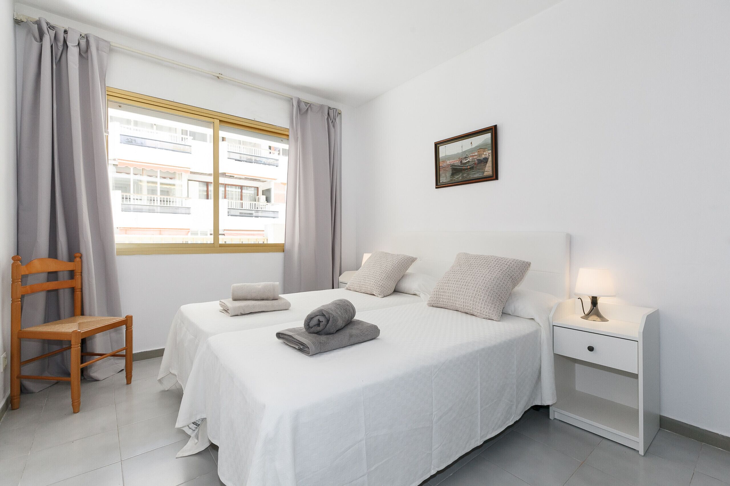 A neatly arranged bedroom with a bed, bedside table, chair, and a window with curtains.