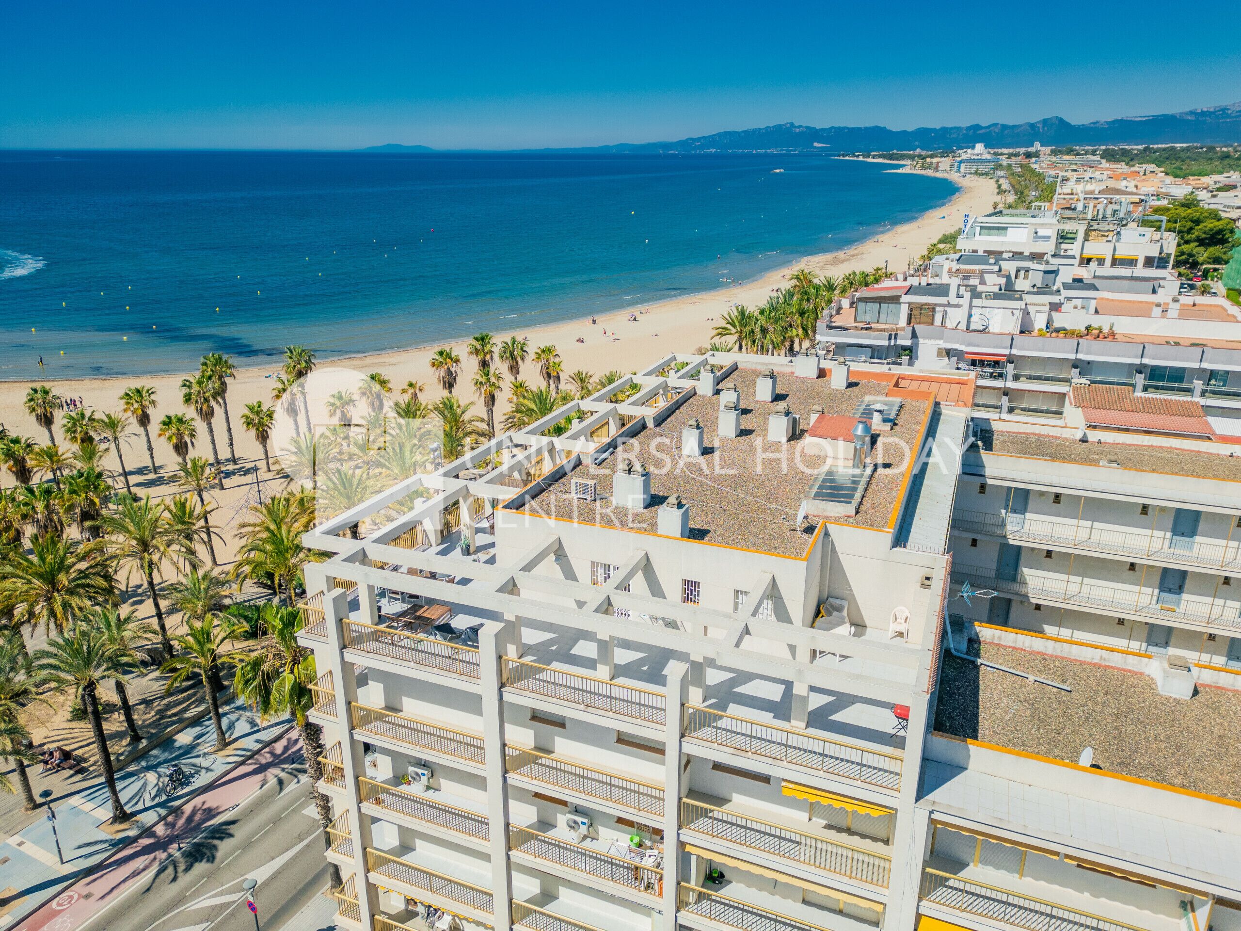 A coastal hotel with multiple balconies, a beach view, and a rooftop terrace.
