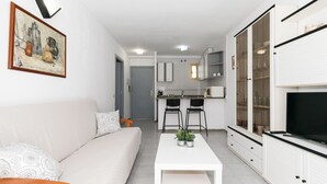 Un salon moderne avec un canapé, une table basse et un téléviseur. Il y a également un coin cuisine avec des placards et un espace repas.