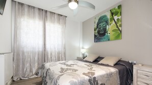 Une chambre à coucher comprenant un lit, des rideaux, une statue de Bouddha fixée au mur, une table de chevet et une petite table d’appoint.