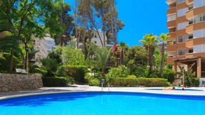 Une piscine entourée d’une végétation luxuriante et un immeuble à plusieurs étages doté de balcons.