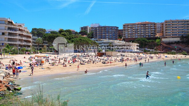 Une plage avec une eau claire, des gens qui prennent un bain de soleil et des bâtiments en arrière-plan.