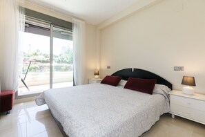 Quarto com uma cama grande, mesa de cabeceira com abajur, uma cadeira e vista para o exterior.