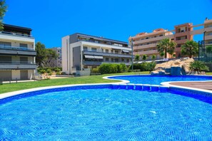 Piscina cercada por edifícios modernos com varandas e um céu azul límpido.