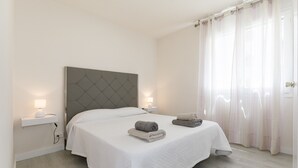 Ein modernes Schlafzimmer mit einem großen Bett, zwei Nachttischen mit Lampen und transparenten Vorhängen.