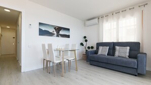 Ein modernes Wohnzimmer mit einem grauen Sofa, einem Glastisch mit weißen Stühlen und einem Elefantenbild an der Wand.