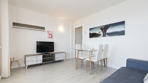 Ein modernes Wohnzimmer mit Flachbildfernseher, einem Esstisch mit Stühlen, einer Couch und einem Gemälde an der Wand.