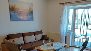 Een woonkamer met een bruine bank, twee grijze fauteuils, een houten salontafel en een schilderij aan de muur.