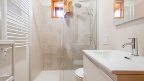 Un baño moderno con ducha de vidrio, un lavabo blanco y un inodoro.