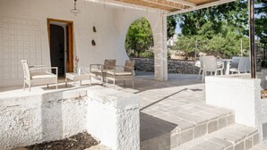Un espacio de estar techado al aire libre con escalones de piedra, paredes blancas y una puerta que da al interior.