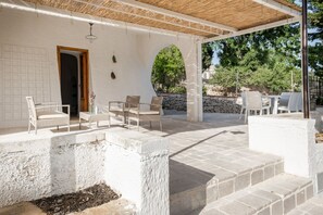 Un espacio de estar techado al aire libre con escalones de piedra, paredes blancas y una puerta que da al interior.