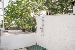 Un mur blanc avec une pomme de douche, un tapis vert et des arbres en arrière-plan.
