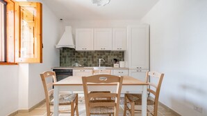 Una cocina con armarios blancos, salpicadero de azulejos, estufa y una mesa de comedor con sillas.
