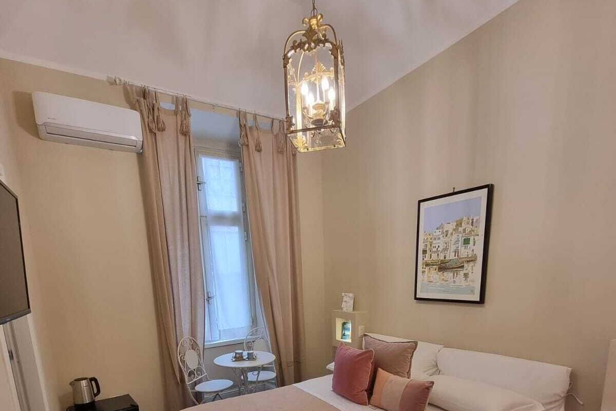 Un dormitorio con cama, una mesa, una silla, una ventana con cortinas y un cuadro en la pared.