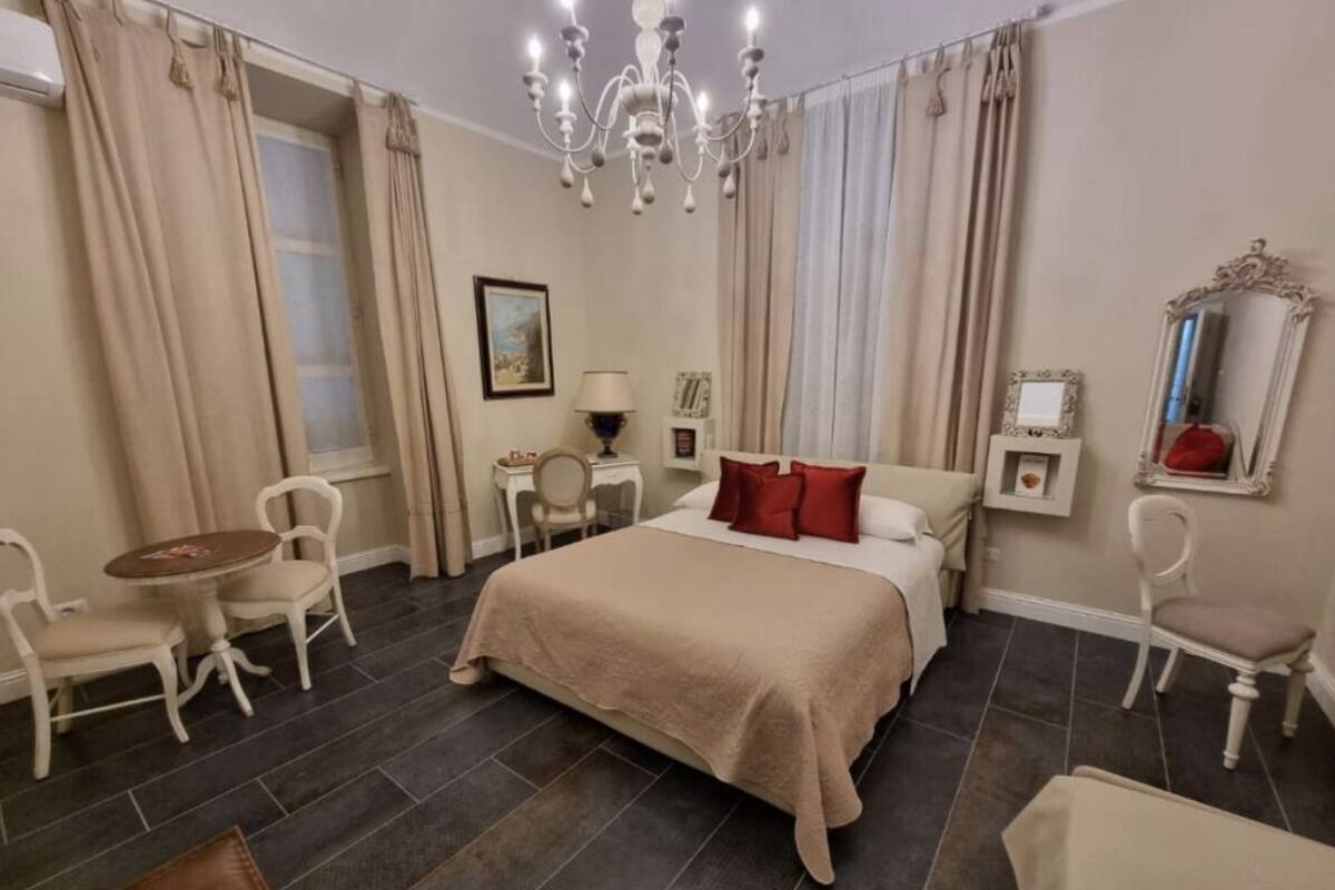 Una habitación de hotel con cama, candelabro, escritorio, sillas y ventana con cortinas.