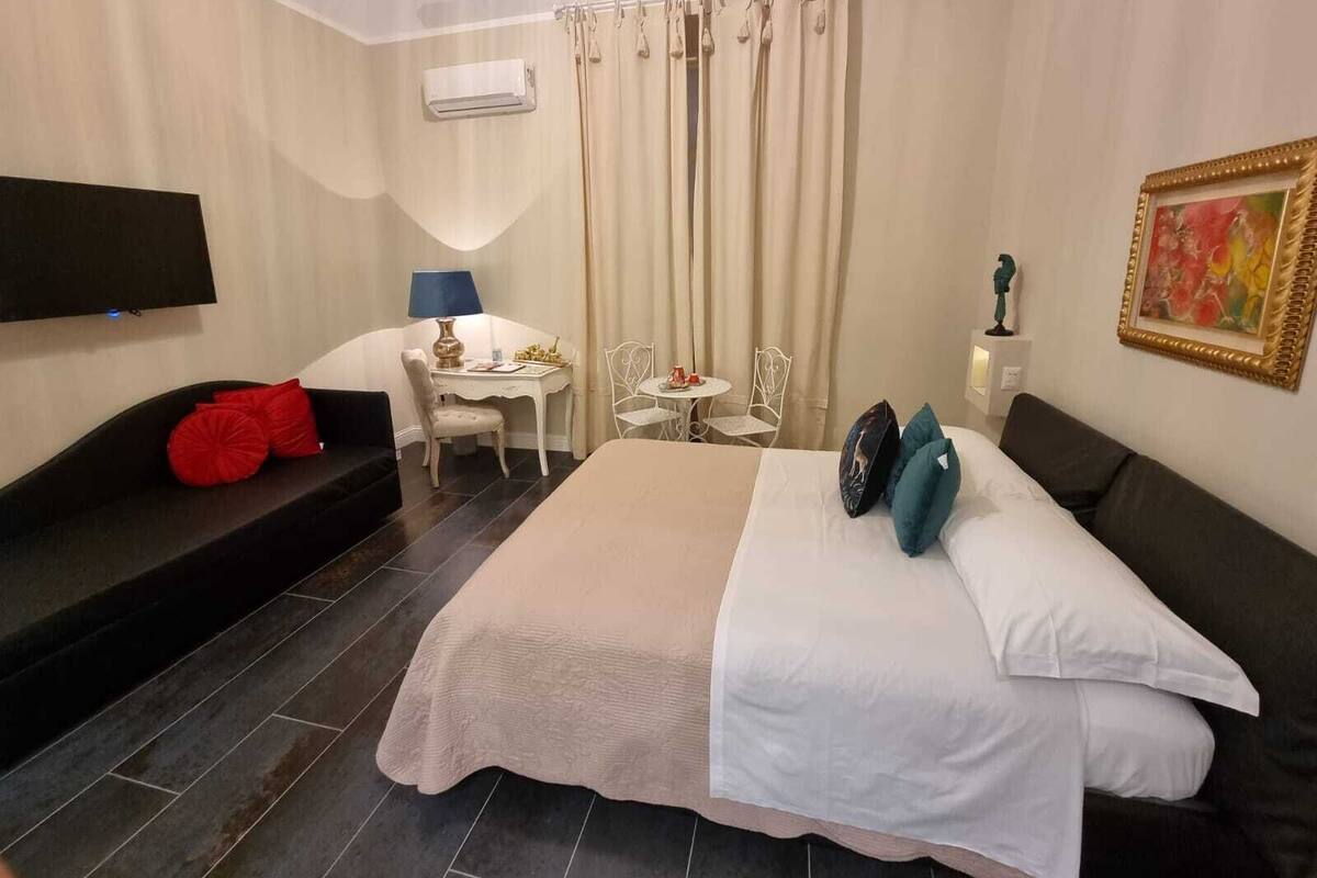 Habitación de hotel con cama, escritorio, silla, televisor y un cuadro.