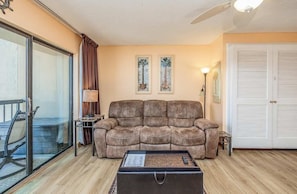 A living room with a brown sofa, a glass door leading outside, a lamp, and a white door with louvered shutters.