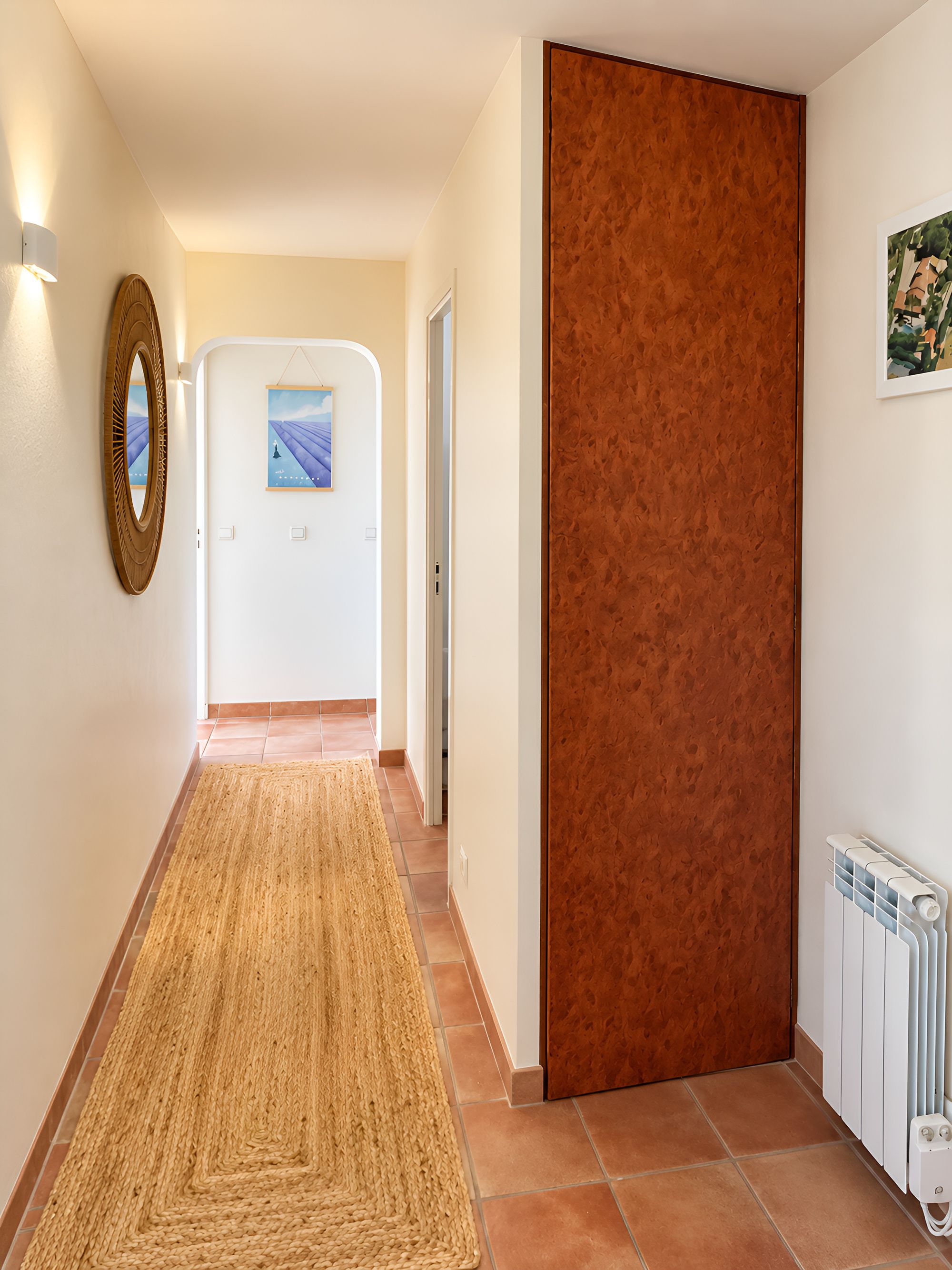 A hallway with a woven rug, a wooden door, and a framed picture on the wall.